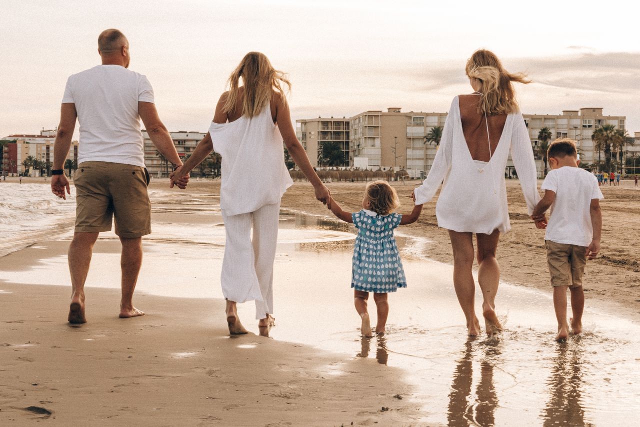 Family with two adults and two young children walking hand in hand along a wet sandy beach at sunset