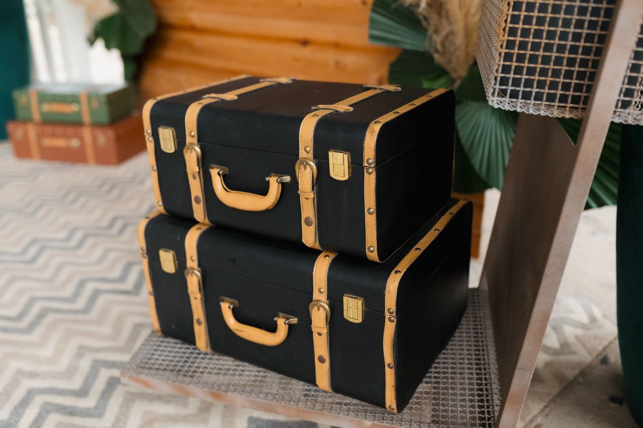 Two black vintage travel trunks with tan leather straps and brass latches stacked on a shelf