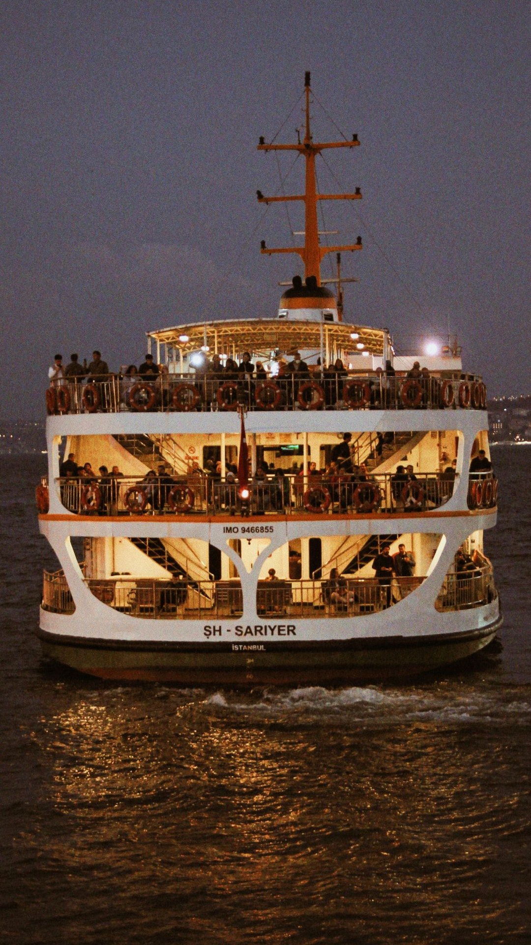 Illuminated multi-deck passenger ferry crowded with people crossing the water at dusk in Istanbul