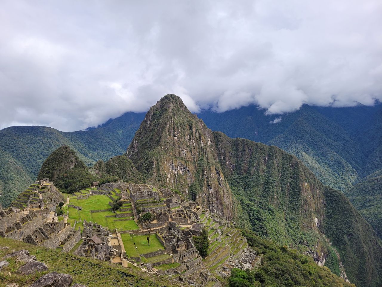 Panoramic view of the Inca citadel of Machu Picchu with Huayna Picchu peak rising through low clouds above green Andean terraces
