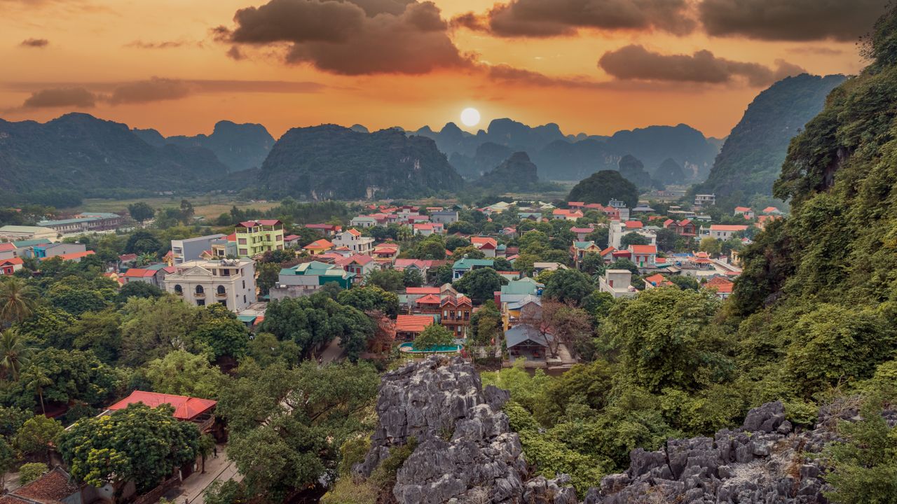 Sunset over a Vietnamese village of red-roofed houses surrounded by limestone karst mountains and dense green trees