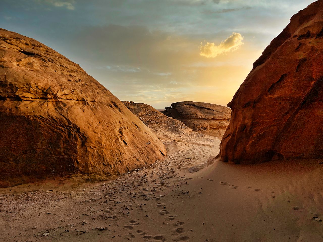Sandy desert path winding between towering red sandstone rock formations at sunset in Saudi Arabia